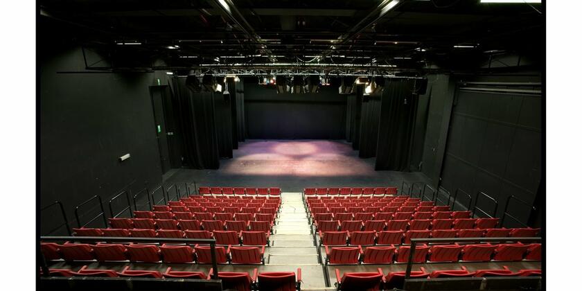Binnenzicht van theater Minnemeers met rijen rode zitjes en een groot podium.