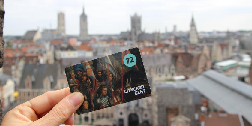 Hand met citycard Gent (72 u) met op de achtergrond de gekende skyline van Gent. (Vanop dak Gravensteen)