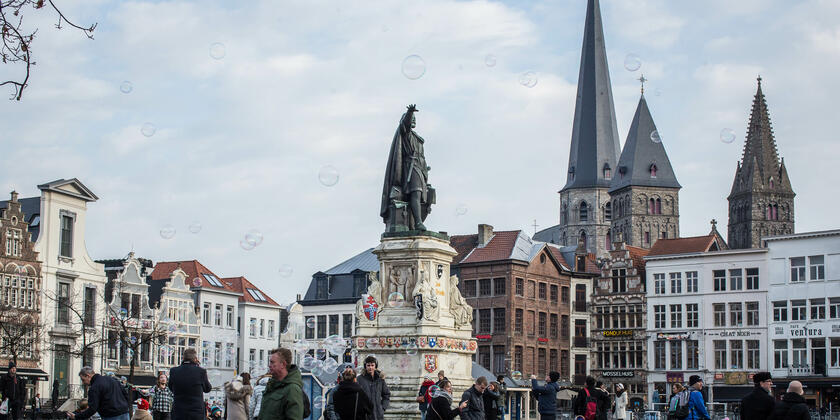 Vrijdagsmarkt (Le Marché de Vendredi) avec des bâtiments médiévaux, en arrière-plan l'église St. Jacob. Au milieu du Vrijdagsmarkt se trouve la statue de Jacob Van Artevelde. Plusieurs personnes se promènent sur le marché.