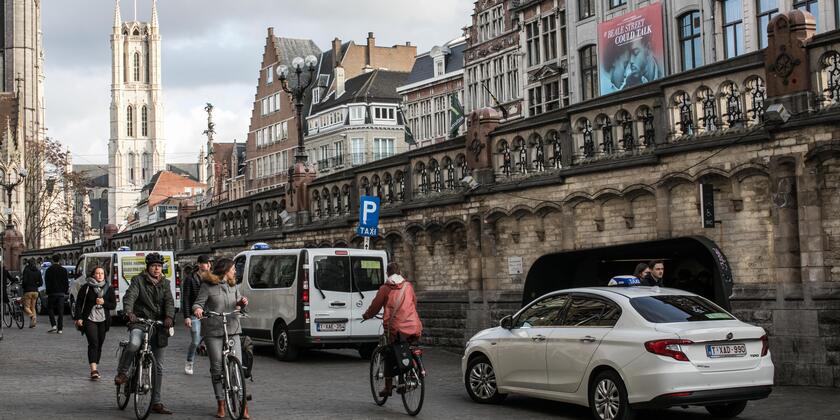 Witte taxi's staan te wachten naast de Sint-Michielsbrug. Voetgangers en fietsers passeren. 