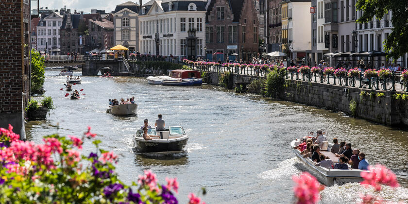 Gent, de Leie, op een zomerse dag. Er zijn plezierbootjes, gegidste boottours en kajaks aanwezig op het water.