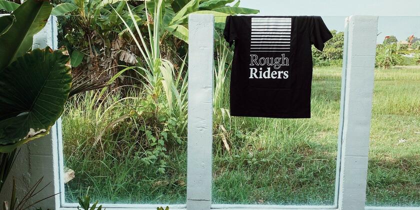 zwart t-shirt met rough riders op die hangt over een terrasafscheiding, veel groen 