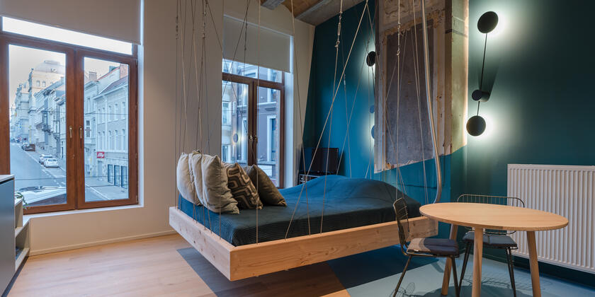 kamer met tweepersoonsbed dat aan het plafond hangt, blauwe en witte elementen, een tafel met 2 stoelen
