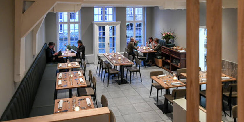 Binnenzicht op het restaurant, grijze banken, natuurhouten tafels voor 2, 4 of meer.