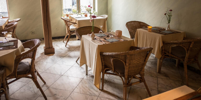 Vierkante tafeltjes met beige tafelkleden en brede rotanzetels, in beige interieur.