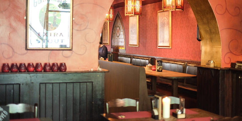 Muren geschilderd in oudroze met zwarte krullen, zitbanken, houten tafels en stoelen, groene lambrisering.