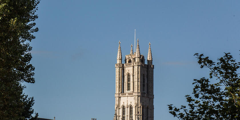 Witte toren van de Sint-Baafskathedraal tegen een staalblauwe hemel.