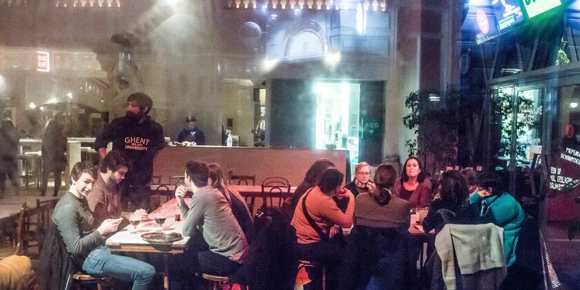 Mensen die in het Vooruit café aan tafels zitten, een lange bar met iemand achter.
