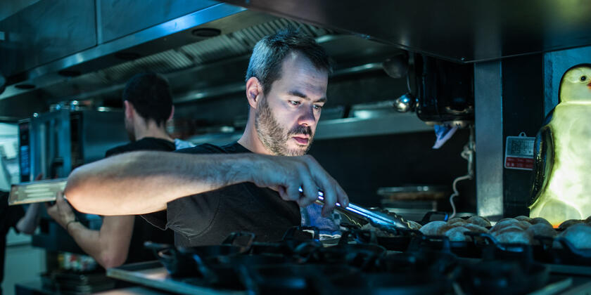 Chef aan het fornuis met grijptang in de hand.