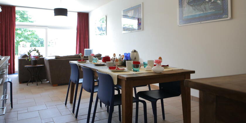 eetkamer met houten tafel, stoelen, gedekt voor het ontbijt, schilderijen aan de muur, zithoek