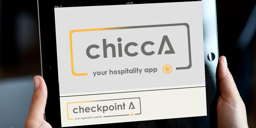 2 handen die een tablet vasthouden met daarop chicca your hospitality app