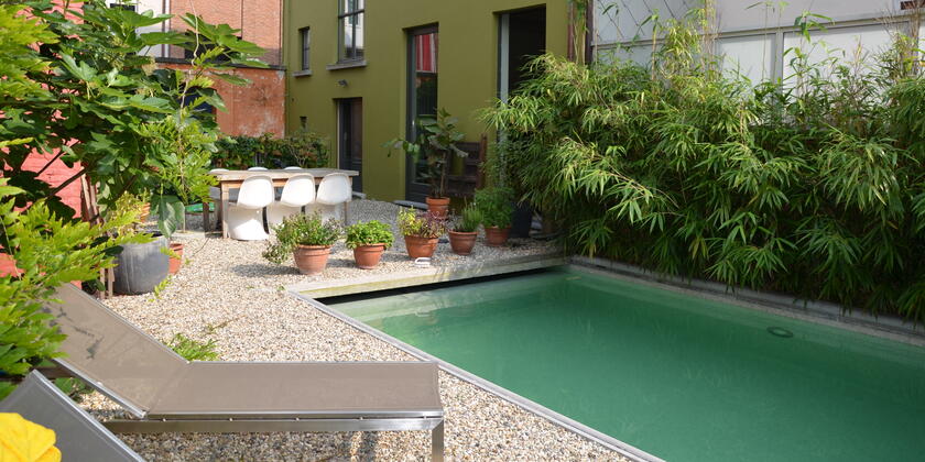 Stadtgarten mit Swimmingpool an einem sonnigen Tag, zwei Liegestühle und ein Tisch mit sechs weißen Stühlen.