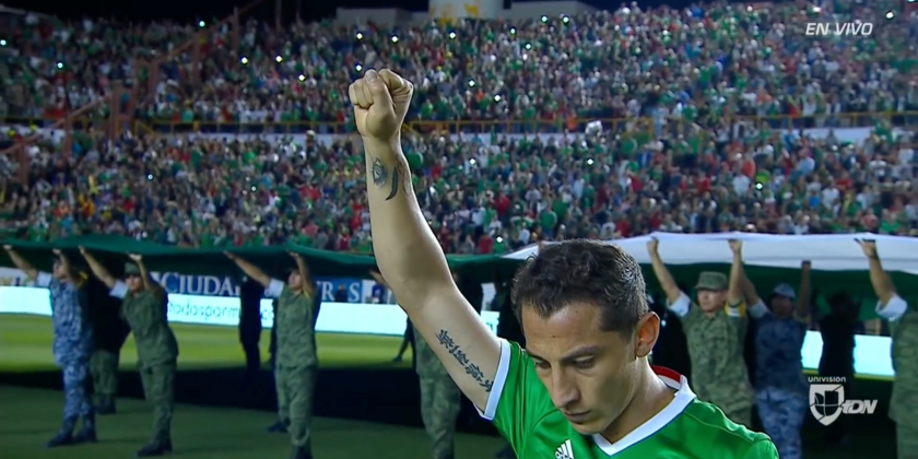 Un footballeur levant la main et une foule qui observent une minute de silence