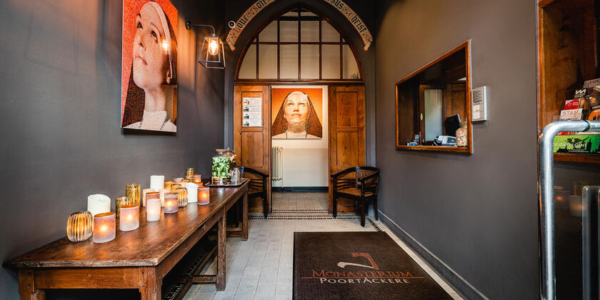 Entrance hall with wooden accents. Along the left side is a wooden table with candles. At the end of the hallway is an illuminated portrait.