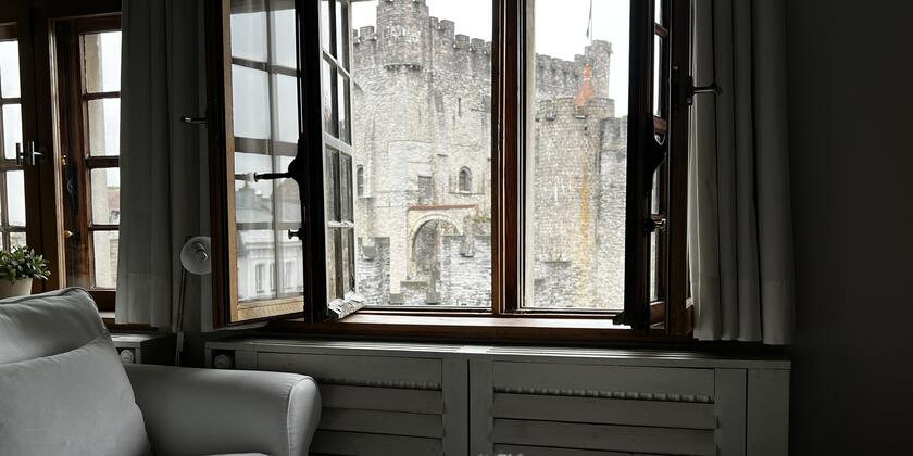 View through the window of a B&B room looking out at a grey castle in Ghent.