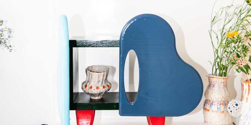 Un grand miroir rond d'un rouge vif au-dessus d'un meuble coloré et ludique. Sur le meuble et à côté de celui-ci se trouvent des vases faits main remplis de fleurs.