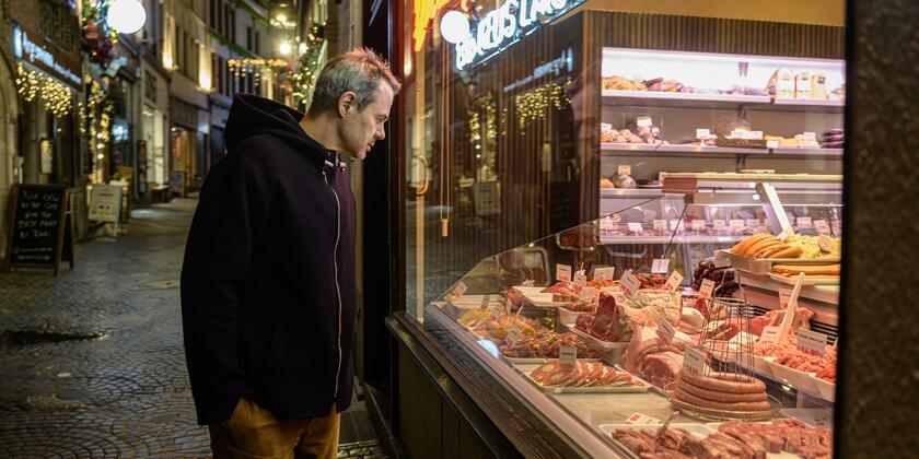 Sterrenchef Olly Ceulenaere kijkt naar vlees in verlichte vitrine van Gentse beenhouwerij bij het vallen van de avond