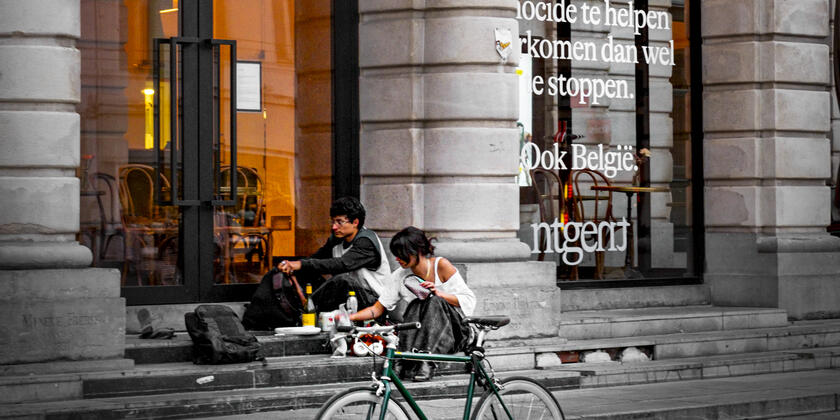 The entrance to a theatre. Two people are having a picnic on the steps at the front. A bicycle is parked at the front.