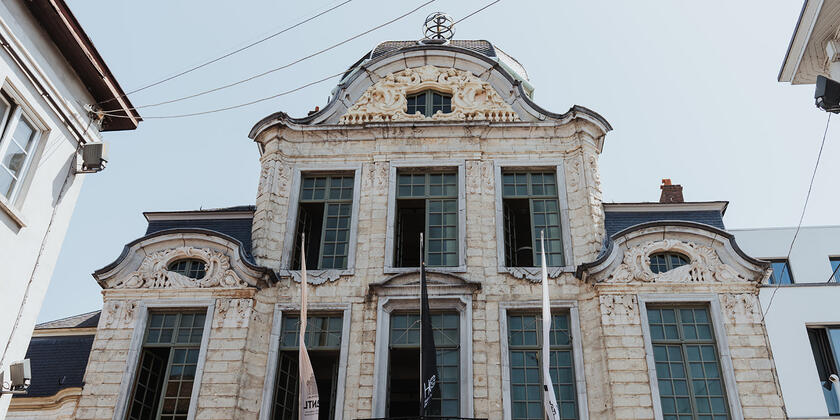 Haus Oombergben. Eine imposante Fassade mit vielen Fenstern, einem kleinen schmiedeeisernen Balkon und drei Fahnen