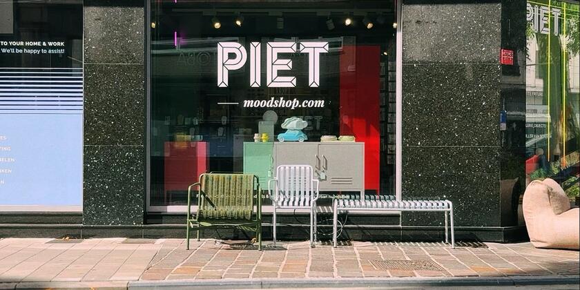 Schaufenster eines Einrichtungsgeschäfts. Auf dem Fenster steht in weißen Buchstaben „PIET moodshop.com“. Vor dem Schaufenster stehen einige Design-Gartenmöbel.