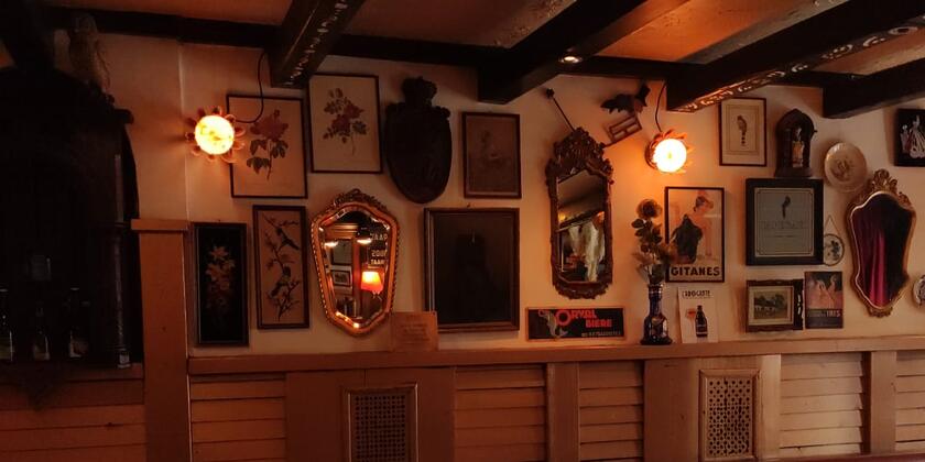 The interior of a café with a floor of black-and-white tiles. Various picture frames and rustic mirrors hang on the wall.