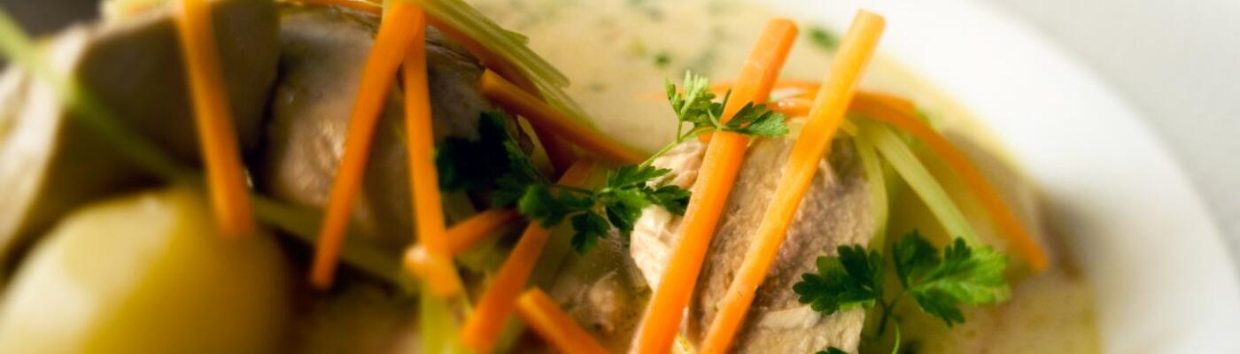 Een bord Gentse waterzooi: aardappelen en kip in een bord met groentesoep. Je ziet wortels, prei en ui, afgewerkt met krulpeterselie.