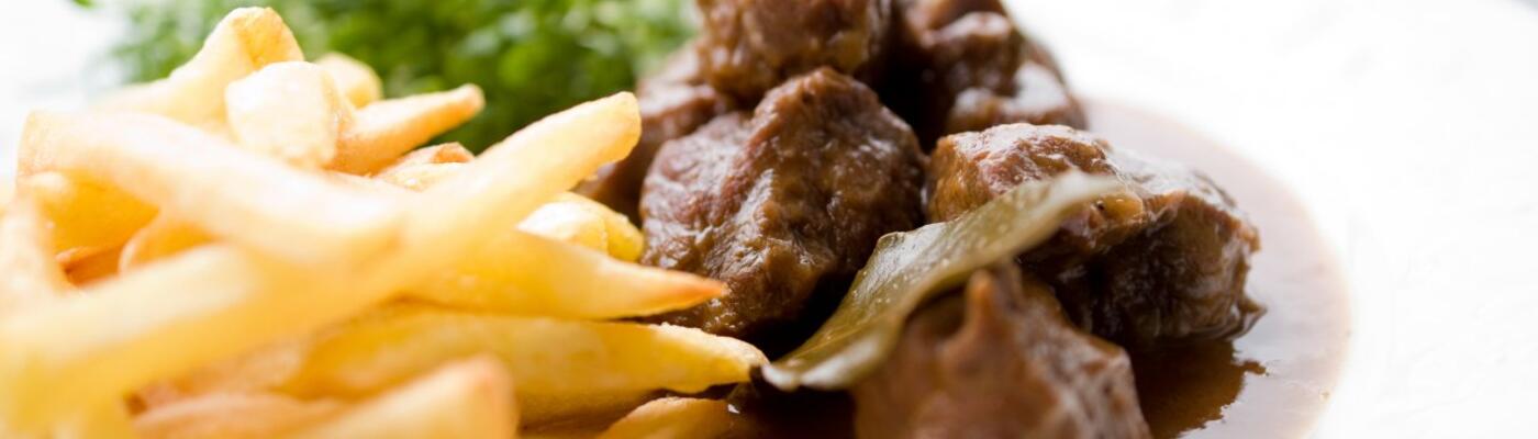 Een wit bord met Belgische frietjes en stoverij: rundsvlees in een bruine saus. Als salade zie je waterkers.