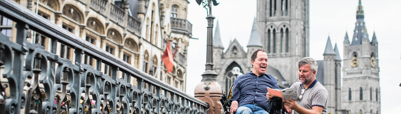 man die uitleg geeft met een boekje aan een man in een rolstoel op de st-michielsbrug