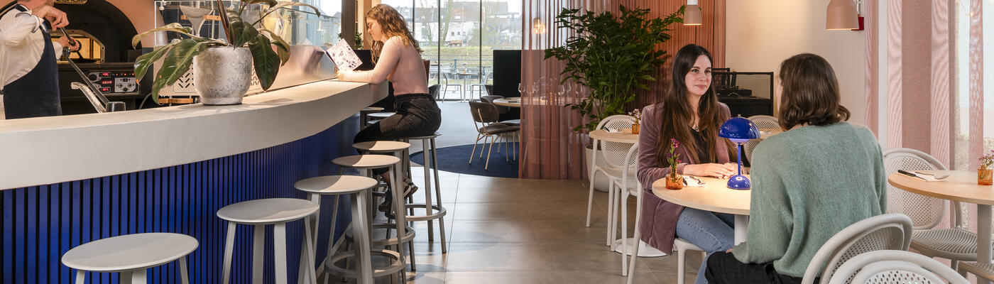 2 women sit at a table on the right and on the left is the bar with pizza oven