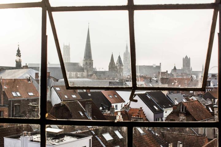 een raam dat openstaat en dat uitkijkt over de daken van Gent