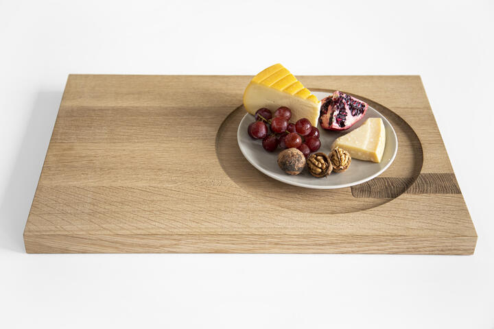 eikenhouten dienblad met daarop een bord met 2 stukken kaas, granaatappel, noten en druiven
