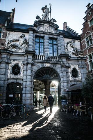 ©VisitGent Barokke poort Oude Vismijn met bovenaan het standbeeld van Neptunus met drietand, links het standbeeld van een man, rechts van een vrouw, door de poort wandelt een koppel de vismijn binnen.