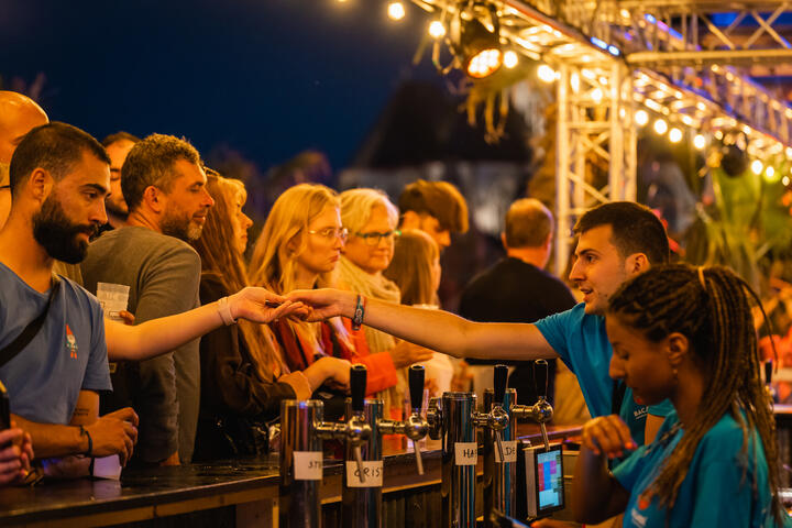 Bezoekers staan aan een verlichte toog en worden bediend door 2 personen