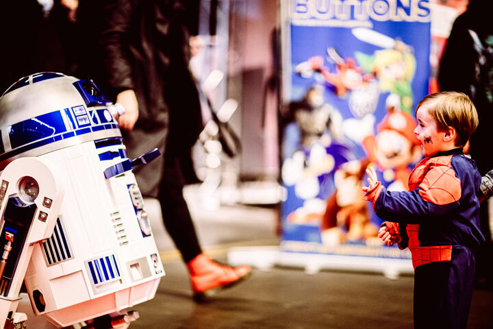 a child dressed as Spiderman waves to R2D2