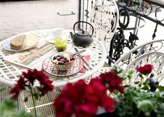 Ontbijt van vers fruit en thee op het terras met Frans smeedijzeren wit tuinmeubilair.