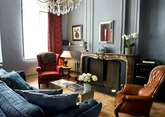 Grote marmeren schouwmantel in de lounge, grijze muren, lederen fauteuils, orchideeën.