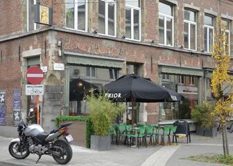 Terras van café Jan van Gent met terrastafels, groene metalen stoelen en zwarte parasols.