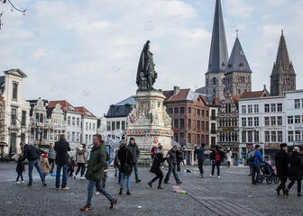 Vrijdagsmarkt (Le Marché de Vendredi) avec des bâtiments médiévaux, en arrière-plan l'église St. Jacob. Au milieu du Vrijdagsmarkt se trouve la statue de Jacob Van Artevelde. Plusieurs personnes se promènent sur le marché.