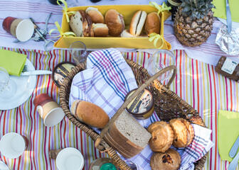 Twee manden gevuld met lokale producten zoals: mattetaarten, sandwiches met hesp, druiven, brood, choco, bier, wijn… op een gekleurd picknickdeken.