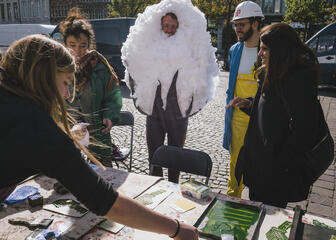 een groep mensen aan een tafel buiten, een man die een kostuum van witte wol aanheeft