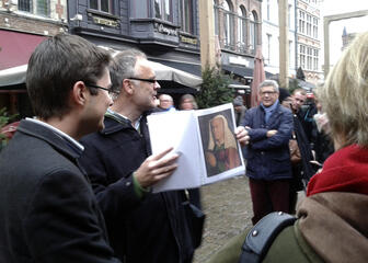 een gids toont een foto van een kunstwerk van Van Eyck uit een map aan zijn groep