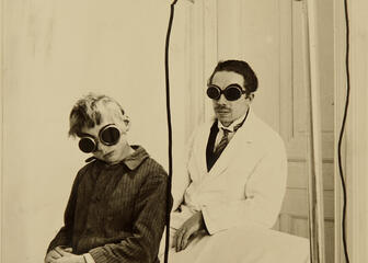 Zwart-wit foto van dokter met jongentje die ronde brillen dragen voor lichttherapie