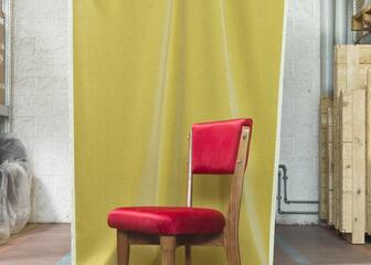 rode stoel met houten poten die voor een geel doek staat