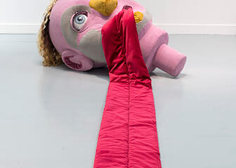 Kunstwerk waarbij een gigantische roze tong uit een roze poppenhoofd hangt