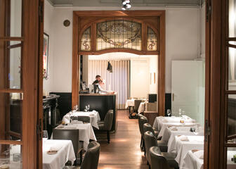 Binnenzicht van restaurant Vrijmoed, met wit gedekte tafels en grijze fauteuils.