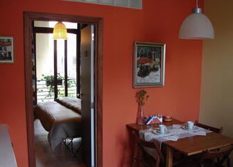 kamer met houten tafel en stoelen, rode muur, deur die uitkomt op slaapkamer, schilderij aan de muur