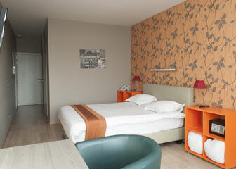 Tweepersoonskamer met grijze muur met oranje accenten.