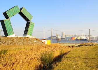 Vergezicht op haven met op de voorgrond een kunstwerk gemaakt uit vier groene containers.