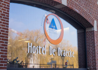 Buitenaanzicht van een raam van Hostel De Draecke met naam en logo.