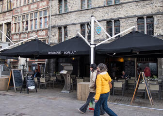 Gevel van restaurant Borluut, in Doornikse breuksteen, terras onder grote zwarte parasols.